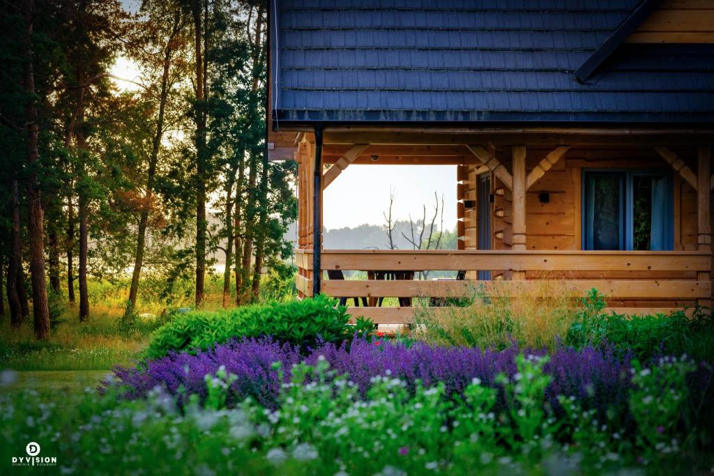 uma cabana de madeira com flores roxas à sua frente em Cisza i wiatr I Nielisz Roztocze em Nielisz