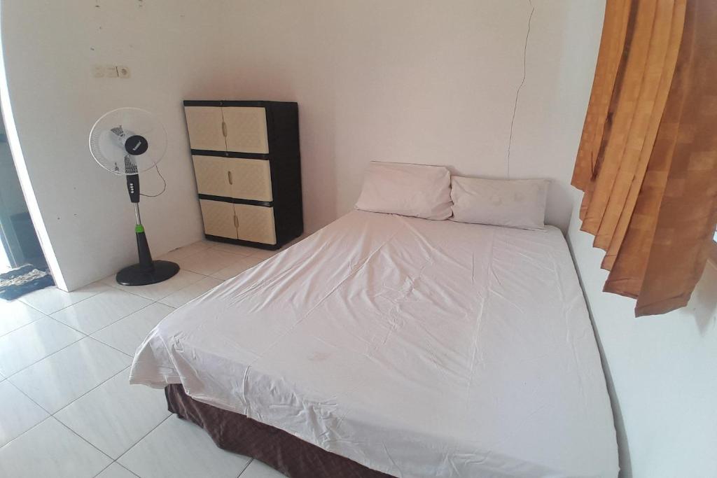 1 dormitorio con 1 cama con sábanas blancas y ventilador en SPOT ON 92738 Wisma Bani Pandi Syariah, en Jepara