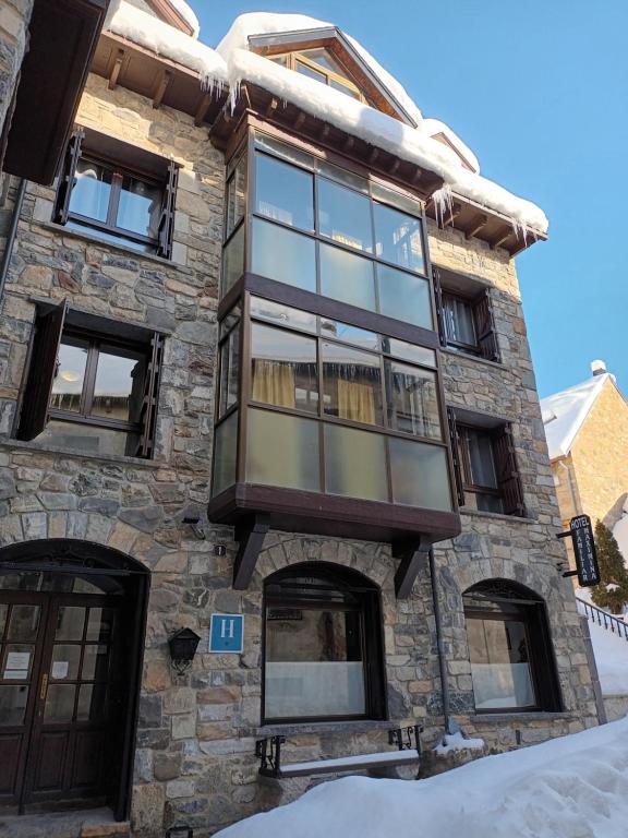 Cette maison en pierre est dotée de fenêtres en verre et d'un balcon. dans l'établissement HOTEL FAMILIAR MAXIMINA, à Sallent de Gállego