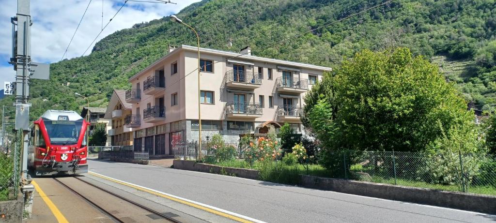 ein roter Zug, der eine Straße entlang fährt, neben einem Gebäude in der Unterkunft Retica Tirano in Tirano