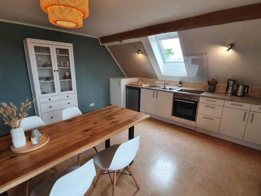 Helle Ferienwohnung - Südeifel في Ammeldingen: مطبخ مع طاولة خشبية وكراسي بيضاء