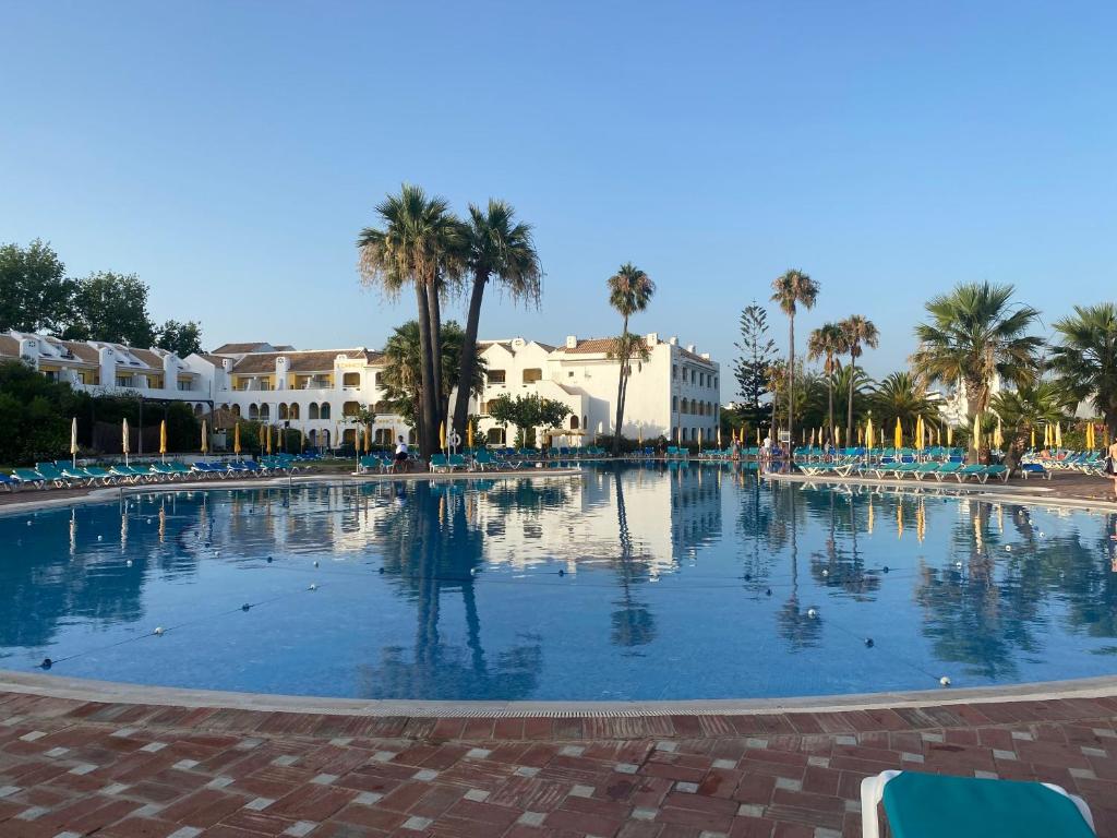une grande piscine avec des palmiers et des bâtiments dans l'établissement Beach House Golden Club, à Cabanas de Tavira