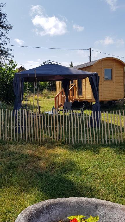 a rv with a blue canopy next to a fence at Roulotte goûteux de nature in Saint-Barthélemy