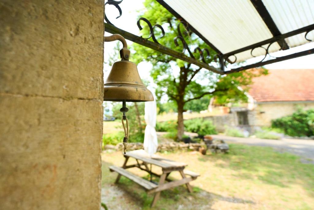 Eine Glocke hängt neben einer Bank im Hof in der Unterkunft La ferme de Roquedure in Montfaucon
