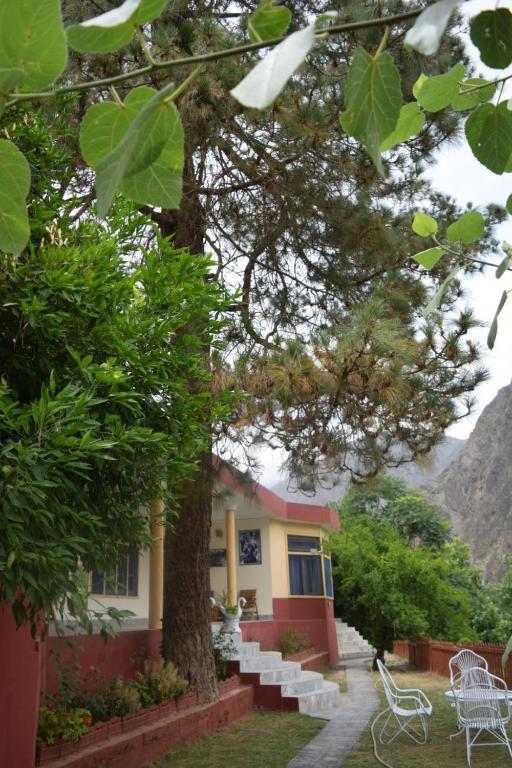 Chitral Green Guest House في شيترال: منزل فيه شجرة وبعض الكراسي البيضاء