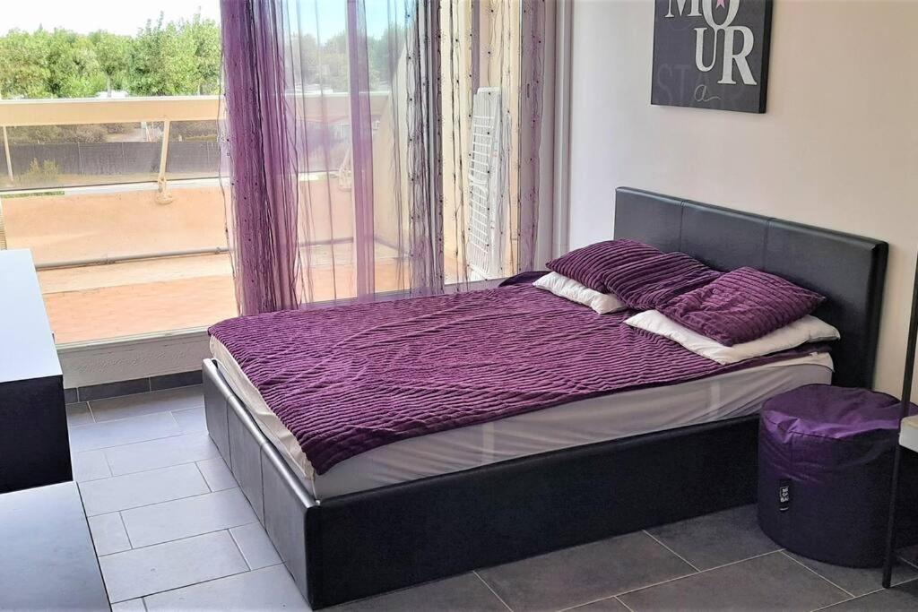 - une chambre avec un lit doté de draps violets et une fenêtre dans l'établissement Studio 77, Héliopolis L au village naturiste, au Cap d'Agde