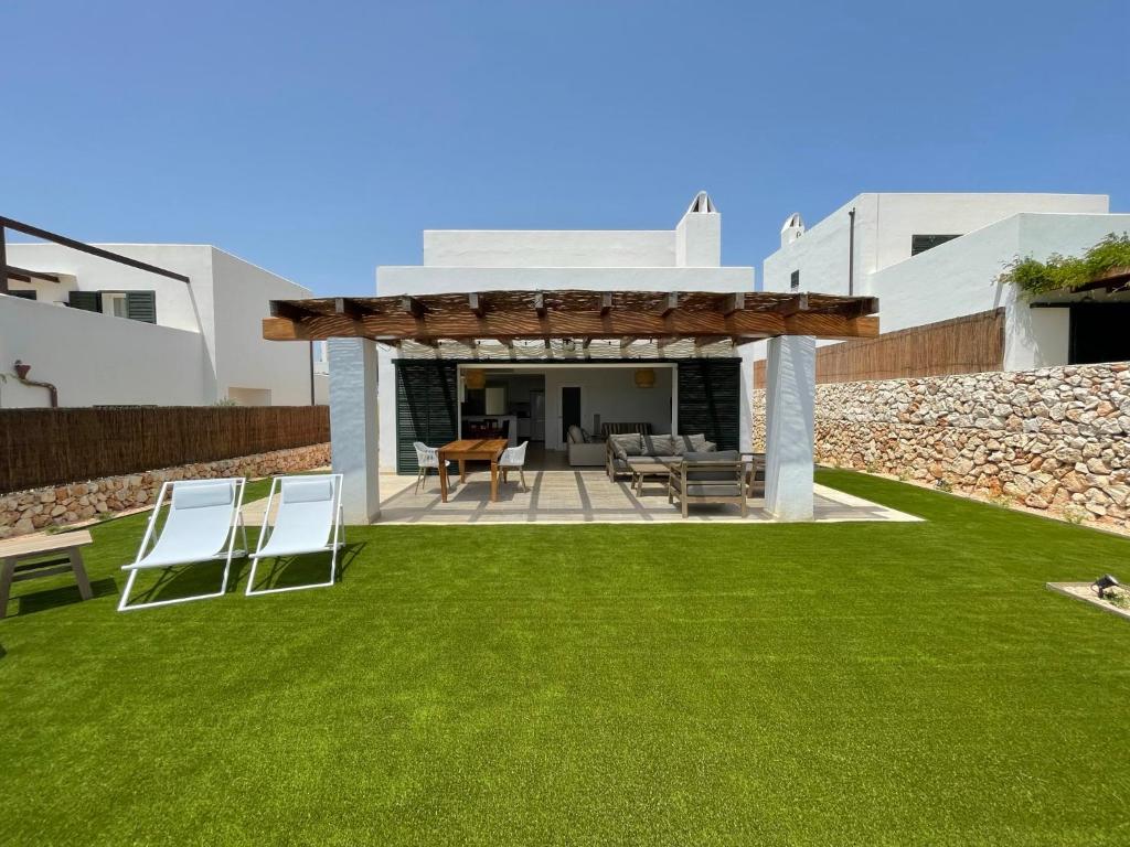 a backyard with green grass and a patio with chairs at Villa Can Simo Menorca in Punta Prima