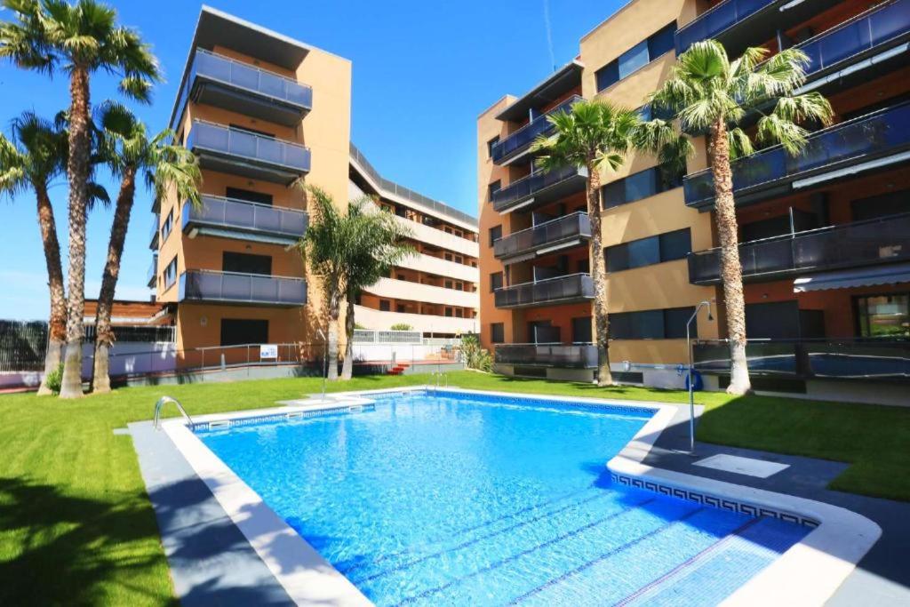 una piscina frente a un edificio con palmeras en Just Oliver Holidays - Amadeus Confort y lujo familiar, en La Pineda
