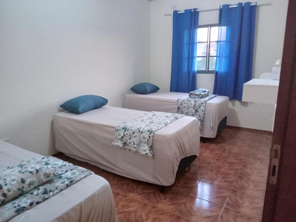 Habitación con 3 camas y ventana con cortinas azules. en Pousada Alvinópolis en Atibaia