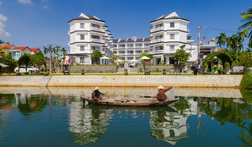 dos personas en un barco en el agua con edificios en Gem Riverside Hotel Hoi An, en Hoi An