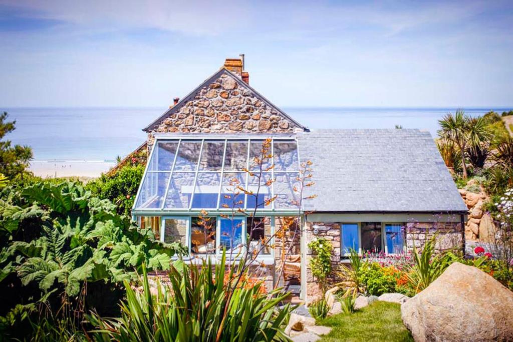 a stone house with a large window on the beach at Castaways, Cottage With Sea Views, Lush Gardens & Patio By the Beach in Sennen