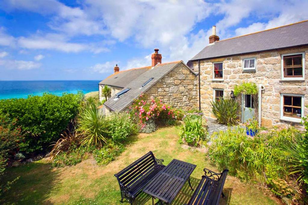 a stone house with a bench in front of the ocean at White Rose, Cornish Cottage With Sea Views & Private Garden By Beach in Sennen