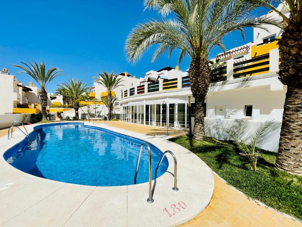 a swimming pool in front of a building with palm trees at Apartamento Vera playa in Vera