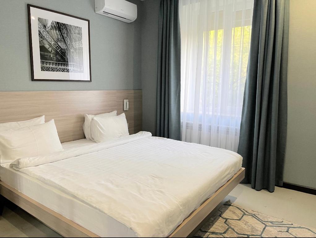 Schlafzimmer mit einem großen weißen Bett und einem Fenster in der Unterkunft Resident Hotel Gogol in Almaty