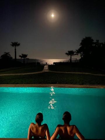 two people sitting next to a swimming pool at night at Ionion Beachfront Villa in Ayia Napa