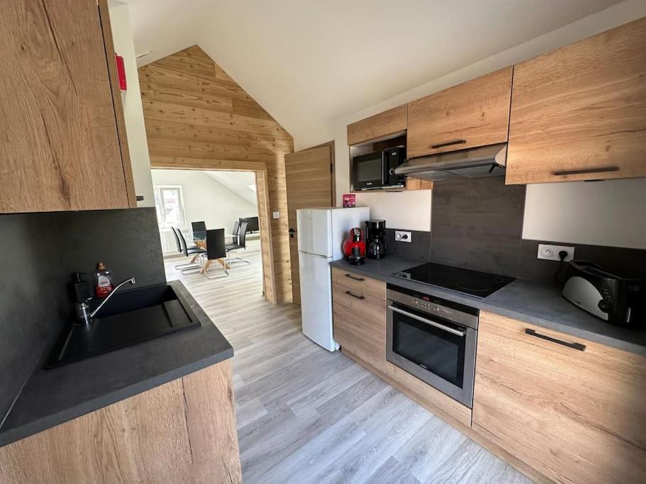 La cuisine est équipée d'un réfrigérateur blanc et de placards en bois. dans l'établissement Appart chez Aurore et Jérôme La Bresse Centre Garage Wifi, à La Bresse