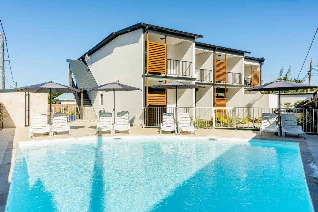 una piscina di fronte a una casa con sedie e ombrelloni di Résidence Touristique LES MASCARINS a Petite-Île