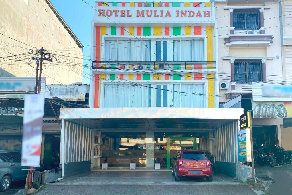 Urbanview Hotel Mulia Indah Palopo في Palopo: سيارة حمراء متوقفة أمام مبنى