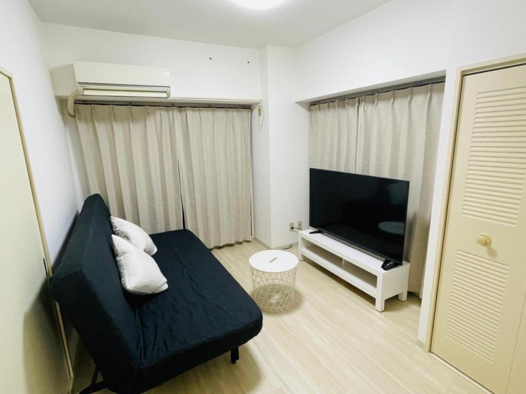 Il comprend un salon doté d'un canapé noir et d'une télévision à écran plat. dans l'établissement ASUKA HINODECHO ｌ日の出町, à Kusugaurachō