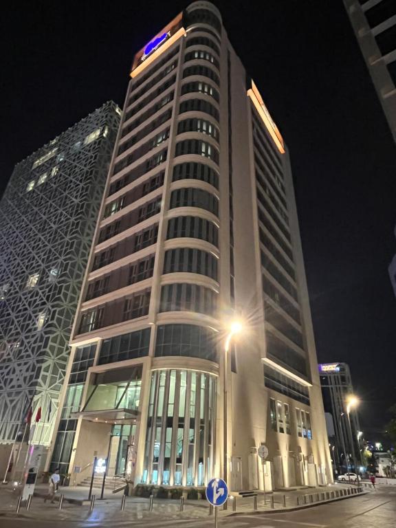 C - Hotel and Suites Doha في الدوحة: مبنى طويل في الليل مع ضوء الشارع في الأمام