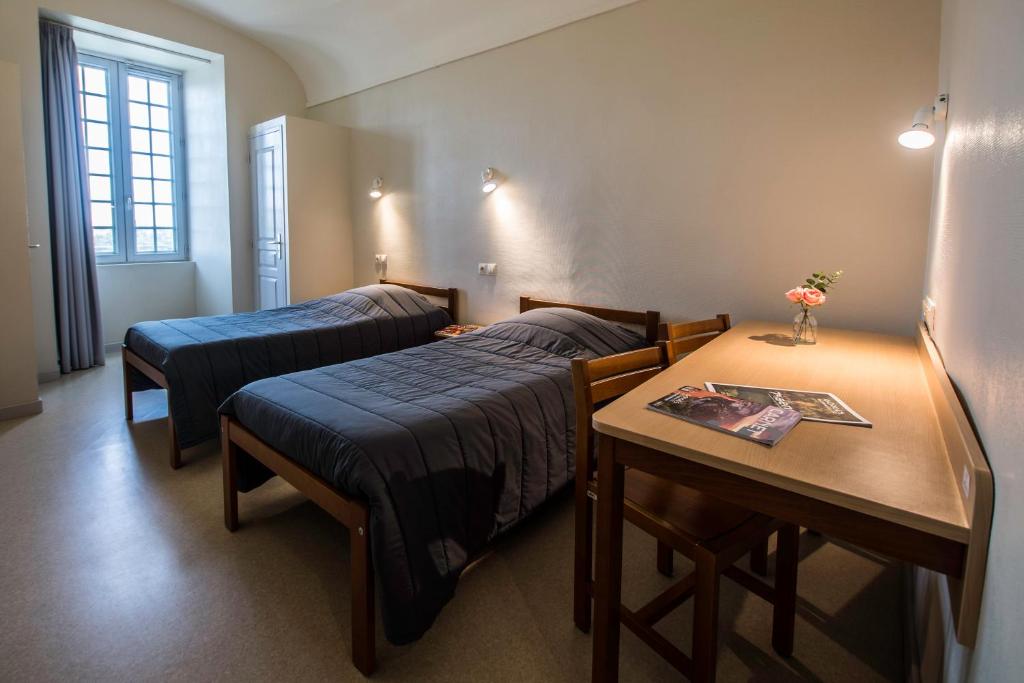 um quarto com duas camas e uma mesa com uma mesa sidx sidx sidx em HOSTELLERIE CHARLES de FOUCAULD em Viviers