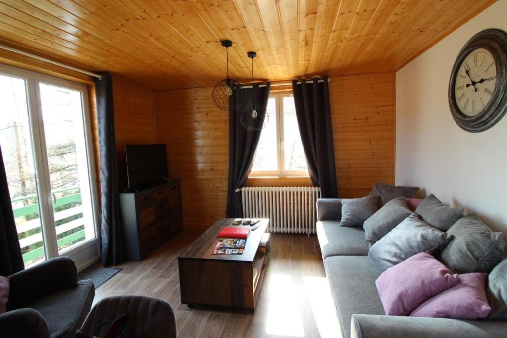 a living room with a couch and a clock on the wall at Apt 1er étage Chalet Au coteau des xette in Gérardmer