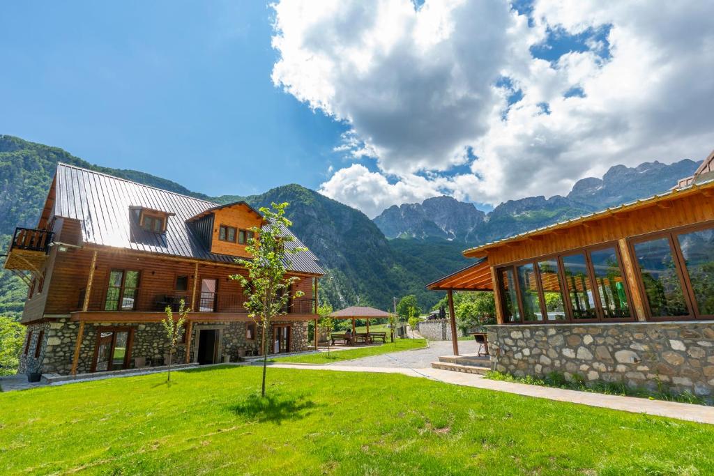 a large wooden house with mountains in the background at Gegest Hotel in Theth
