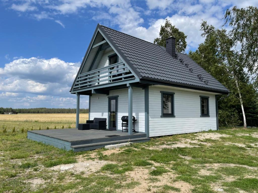 een klein wit huis met een terras in een veld bij Domek Pod Brzozami 