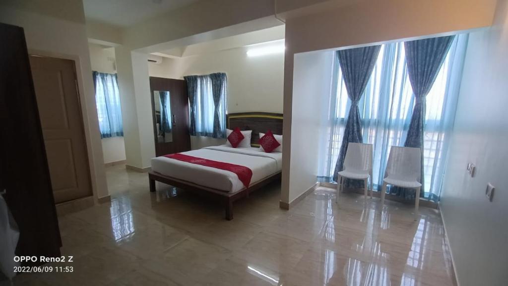 a bedroom with a bed and two white chairs at Hotel Amulya Relax Inn in Bangalore