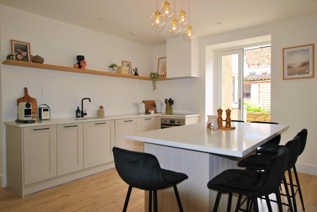 a kitchen with white cabinets and a island with black chairs at Crows Neuk- fabulous coastal family home in Saint Monance