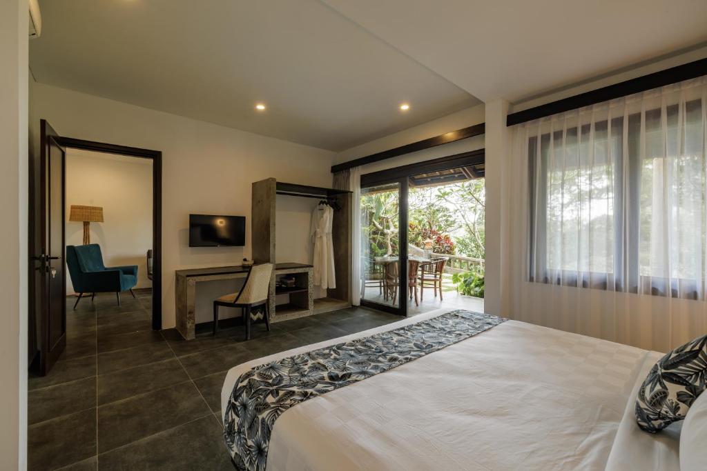 a bedroom with a bed and a desk and a window at Ubud Dedari Villas in Ubud