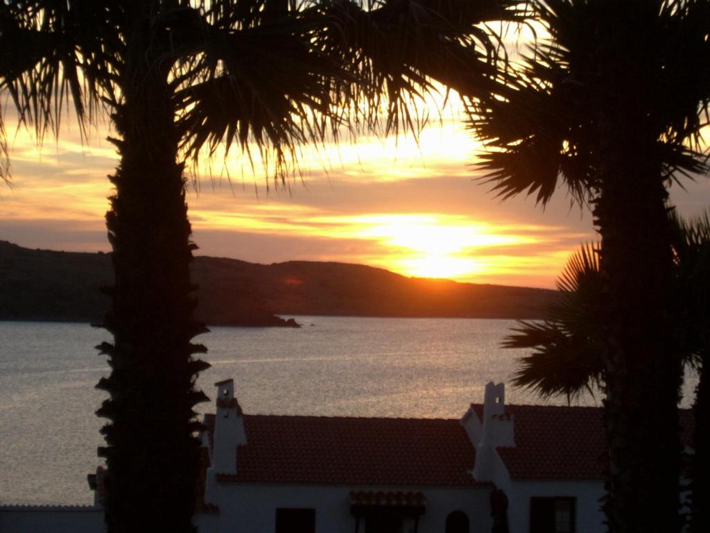 a sunset over the water with palm trees at Apartamentos El Bergantin Menorca Club in Fornells