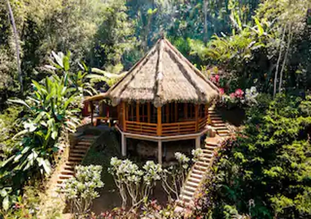 una pequeña casa con techo de paja en un jardín en Bali Jungle Taksu, en Tampaksiring