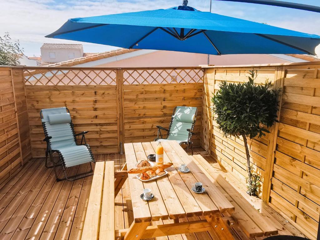 une terrasse en bois avec un parasol bleu et deux chaises dans l'établissement Le Ptit Chaumois - 4 personnes, à Les Sables-dʼOlonne