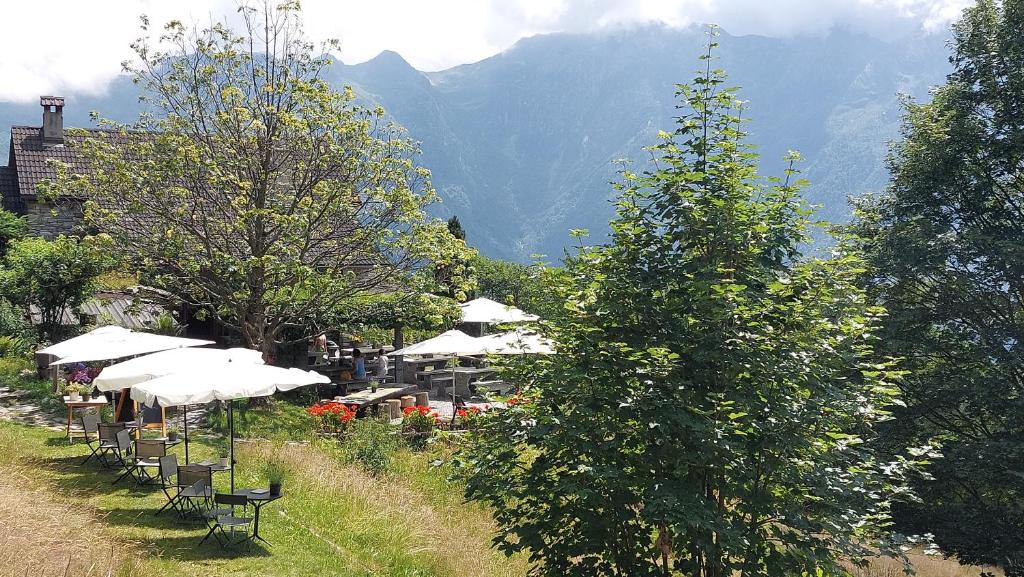 eine Reihe von Tischen und Sonnenschirmen mit Bergen im Hintergrund in der Unterkunft Alla Capanna in Verdasio