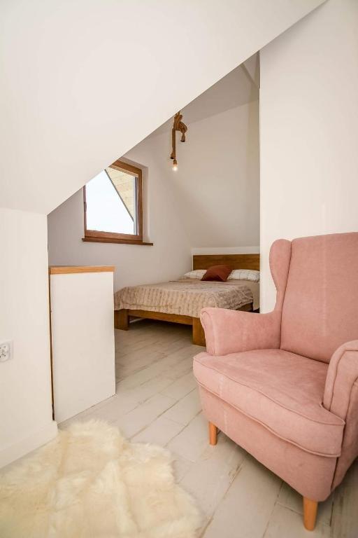 a living room with a pink chair and a bed at Domek za rondem in Ratułów