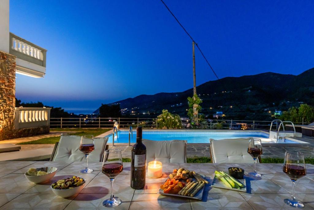 einen Tisch mit Weingläsern und Speisen sowie einen Pool in der Unterkunft Villa Pavlos in Skopelos