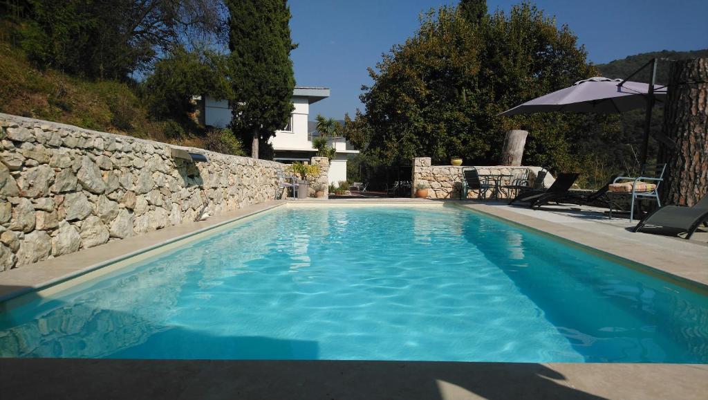 una piscina azul con una pared de piedra y una sombrilla en Le Domaine de la Feuilleraie, en Coaraze