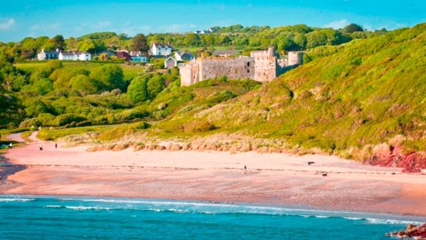 a beach with a castle on top of a hill at Manorbier Castle Inn Sunset Room in Tenby