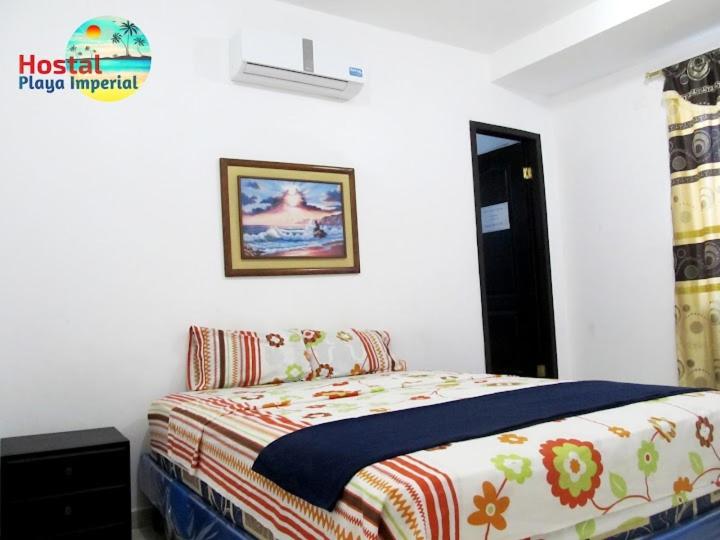 Hostal Playa Imperial Manta في مانتا: غرفة نوم بسرير وصورة على الحائط
