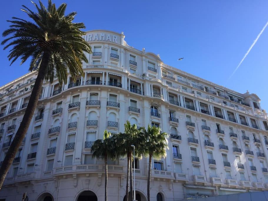 a large white building with palm trees in front of it at Palais Miramar - Suite White Jardin - 20m Plage in Cannes