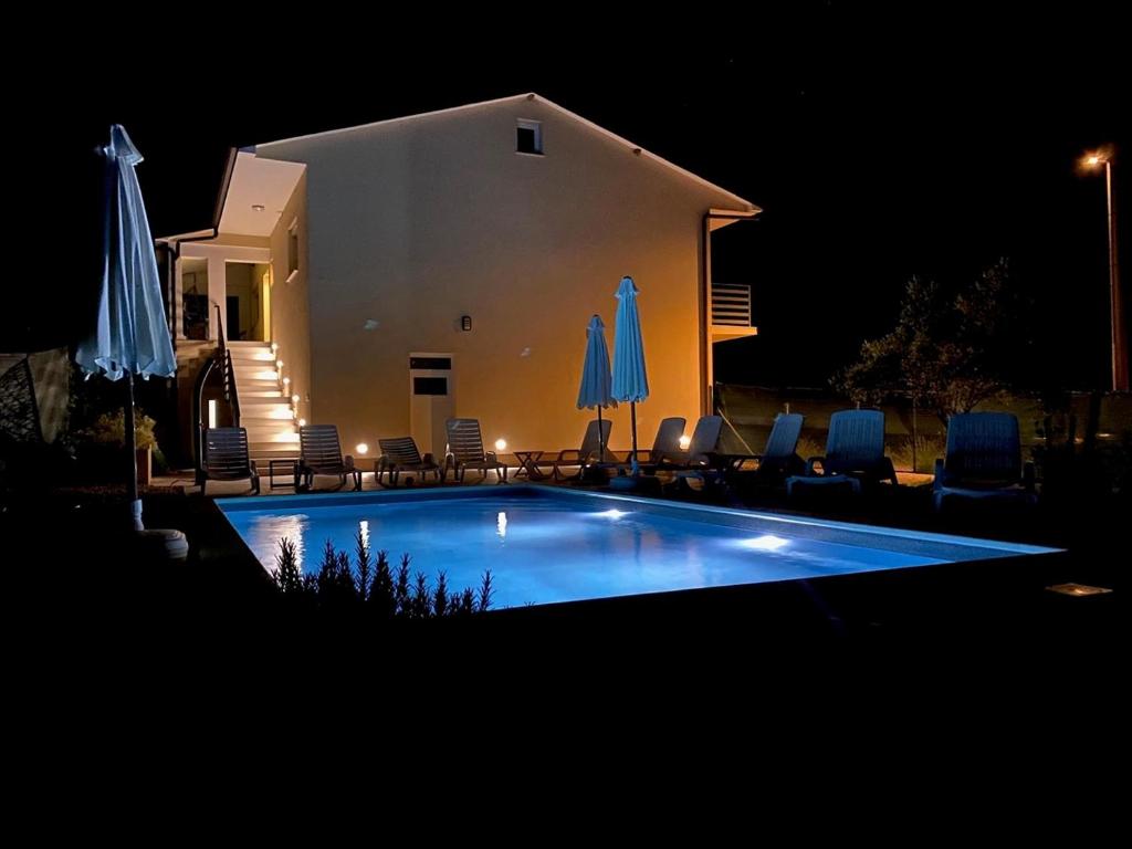 a swimming pool at night with chairs and umbrellas at Apartman Butoniga Nature in Buzet