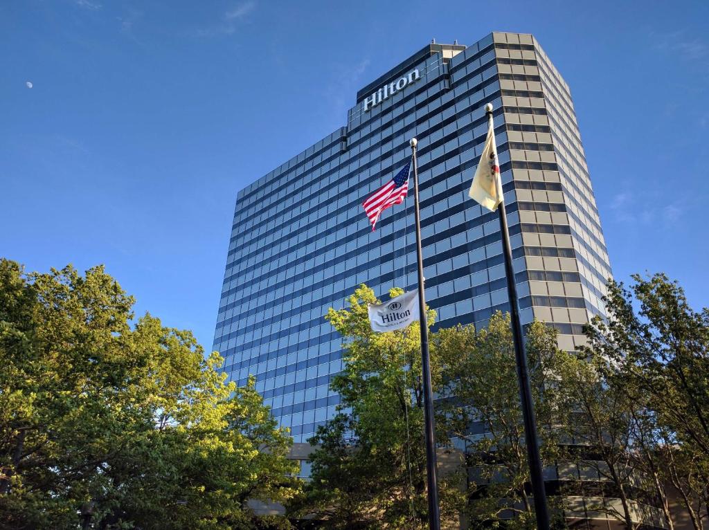 deux drapeaux battant devant un grand bâtiment dans l'établissement Hilton Meadowlands, à East Rutherford