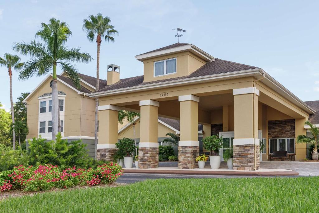 a large yellow house with palm trees and grass at Homewood Suites by Hilton Fort Myers in Fort Myers