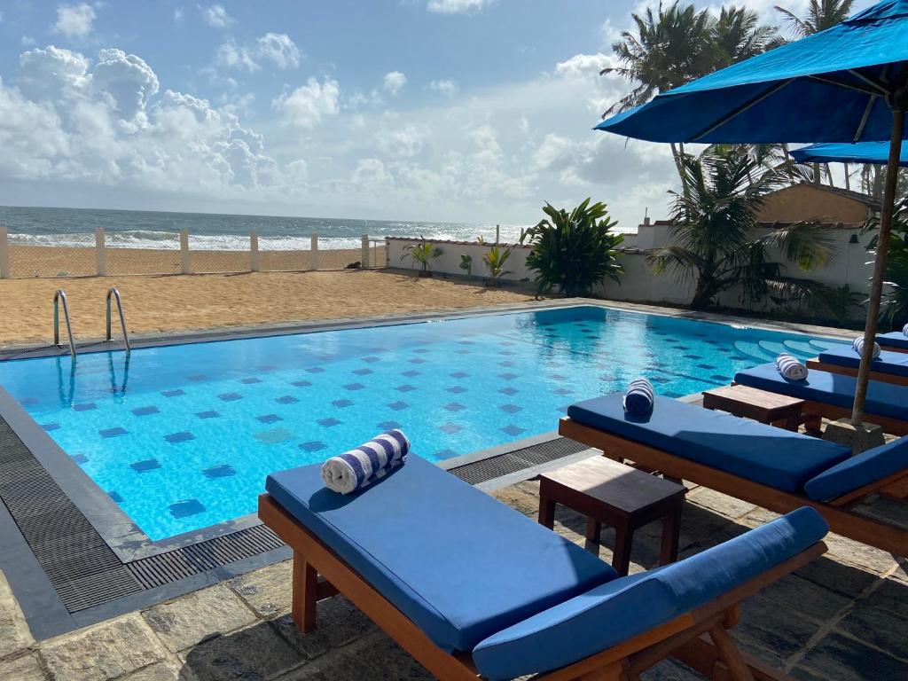 a large swimming pool with chairs and a beach at Tropical Beach House Hikkaduwa in Hikkaduwa