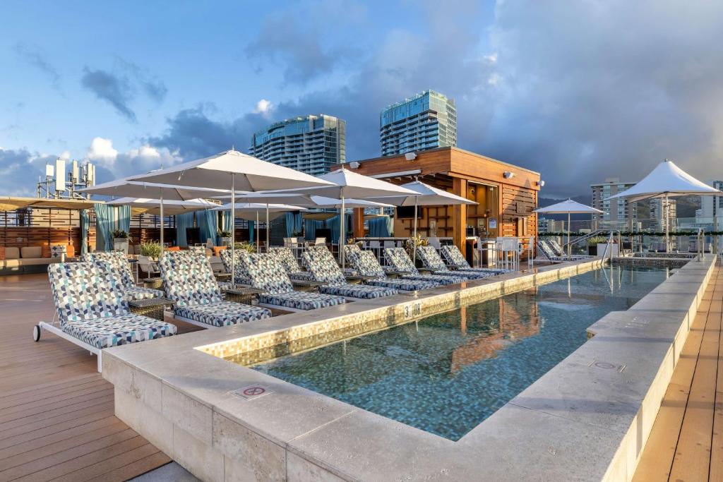 ホノルルにあるHilton Grand Vacations Club Hokulani Waikiki Honoluluの建物内のプール(椅子、パラソル付)