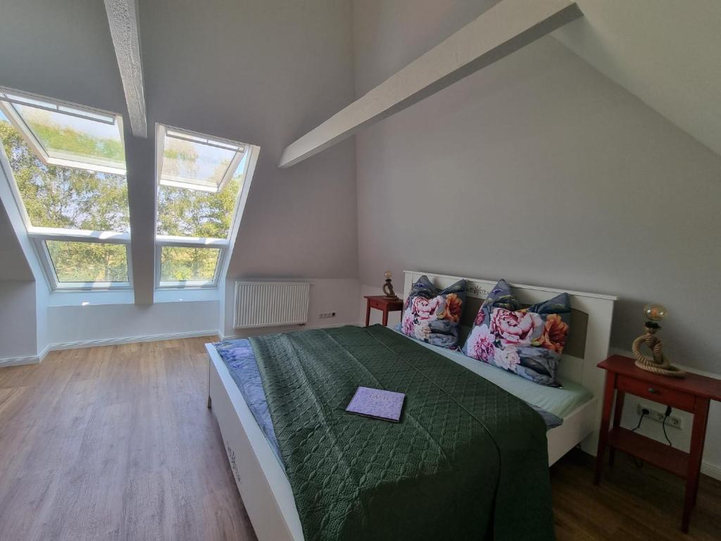 a bedroom with a bed with a green comforter and two windows at Ferienhaus Am Fehntjer Tief in Emden