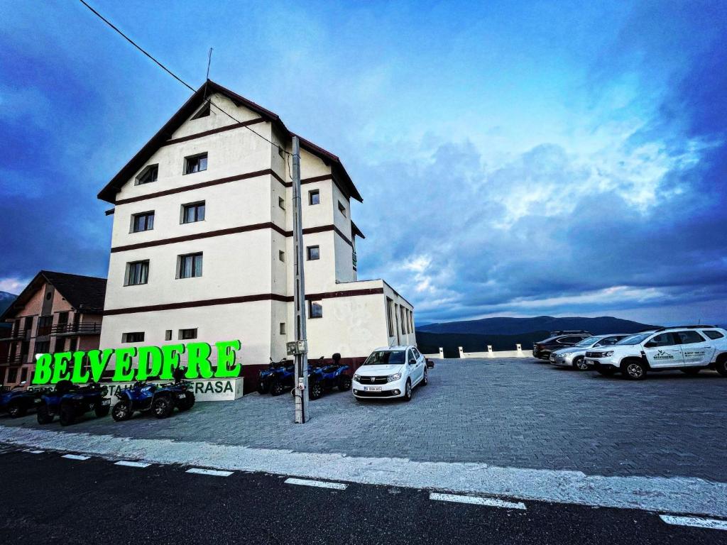 a white building with cars parked in a parking lot at Pensiunea Belvedere in Ranca