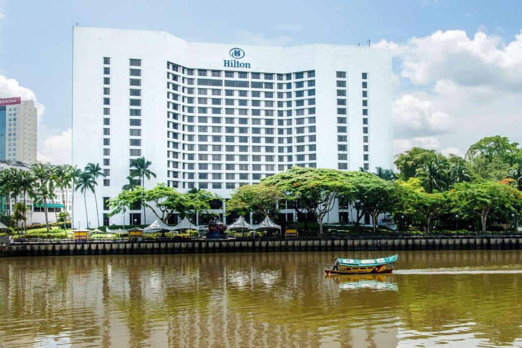 a boat in the water in front of a hotel at Hilton Kuching Hotel in Kuching
