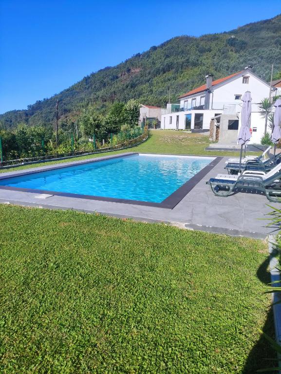 a swimming pool with two lawn chairs and a house at Gerês Home Nature in Geres